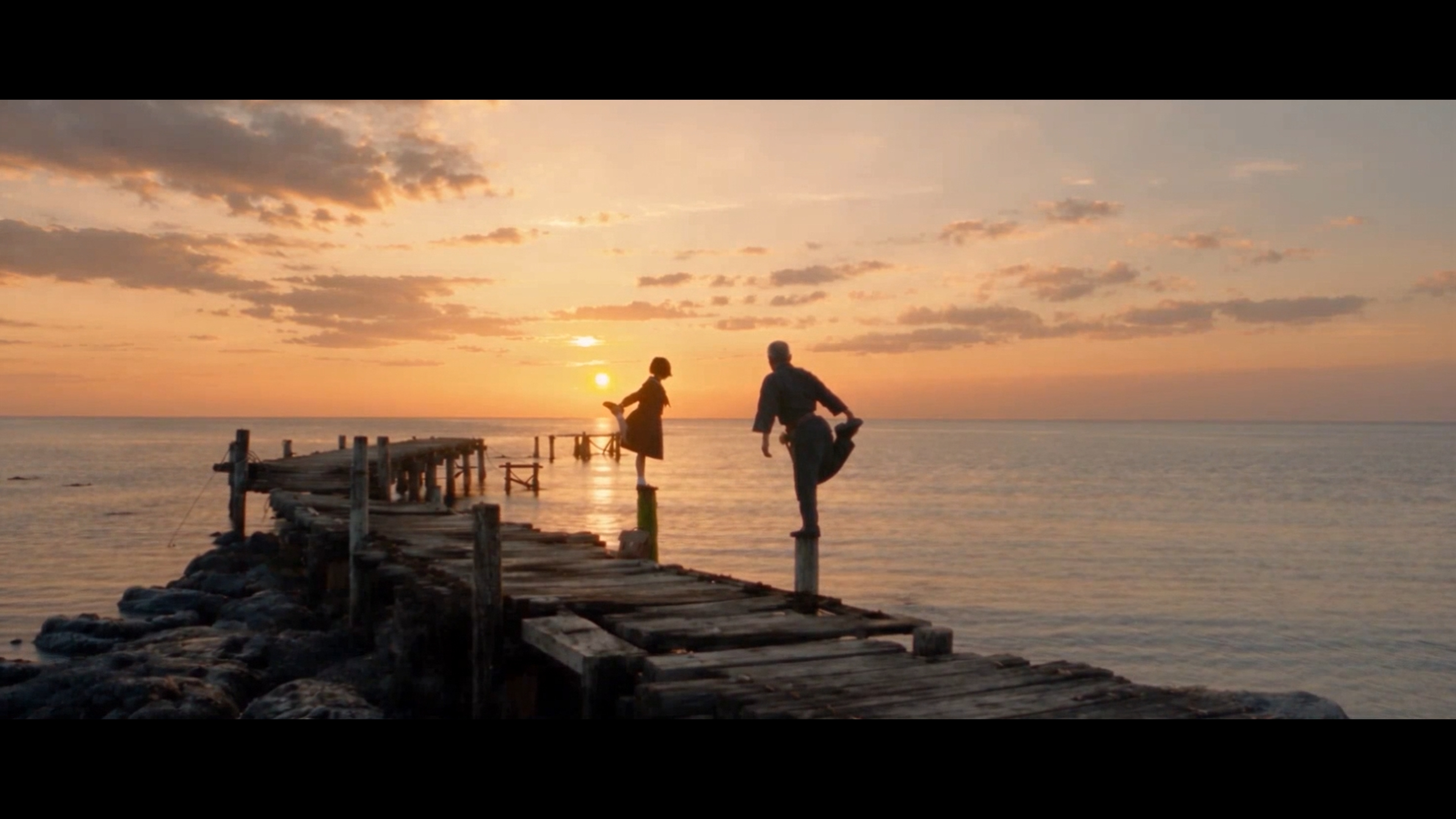 Mayumi and her father balancing on the wooden pier at sunset